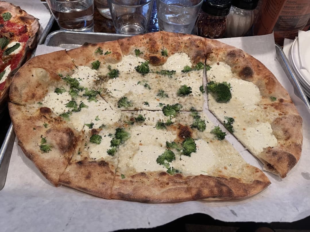 Thin round personal size white pixzza with broccoli and regatta cheese