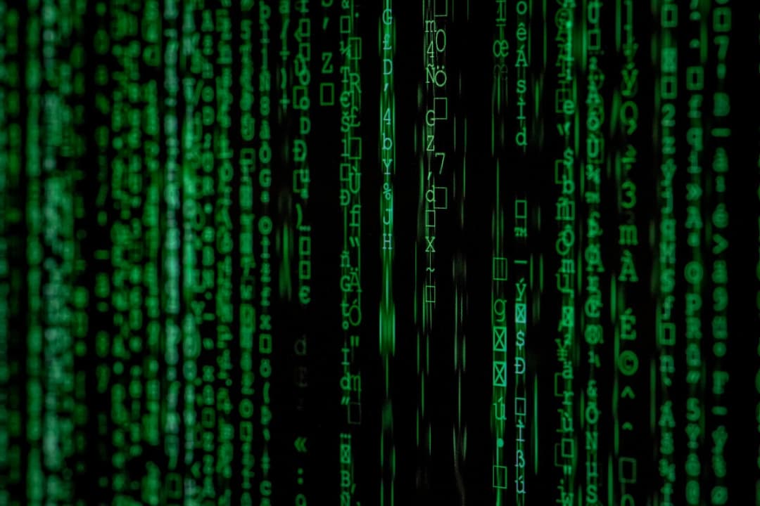 Matrix-style green code streams vertically on a dark background, with various symbols and characters creating a digital, futuristic aesthetic.