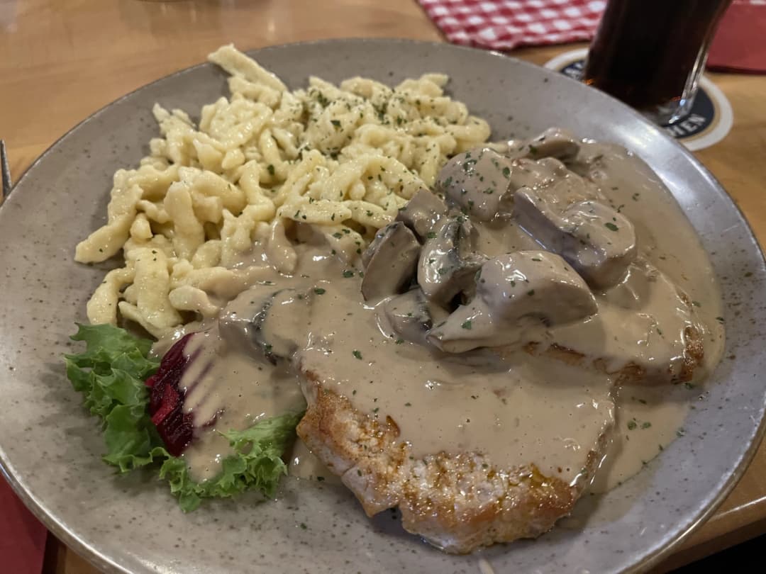 A hearty plate of Jägerschnitzel, a pork steak topped with creamy mushroom sauce, served with a fresh mixed salad and lemon garnish.