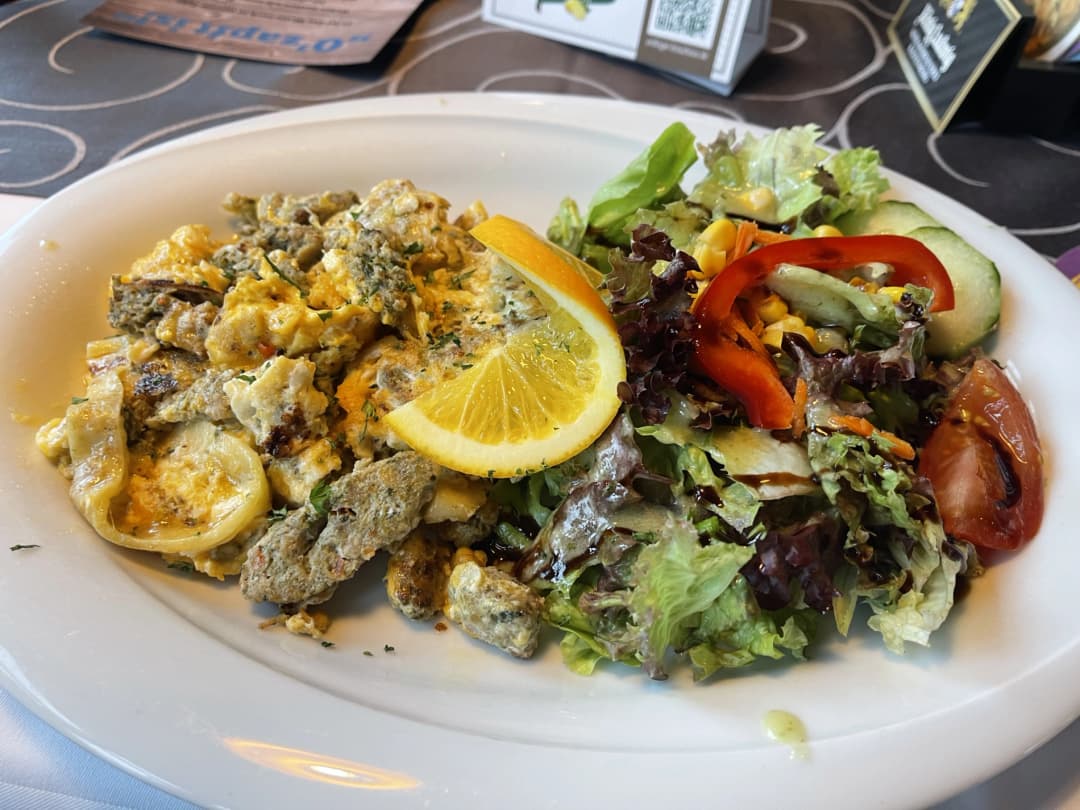A plate of Maultaschen fried with eggs, served alongside a fresh mixed salad with lettuce, corn, red peppers, cucumbers, and tomatoes, garnished with a slice of lemon.