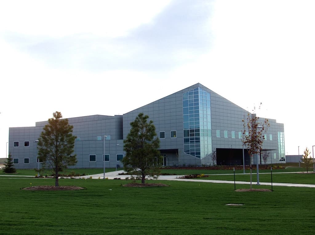 The modern, angular gray building of the U.S. Army Space and Missile Defense Command (USASMDC), home to the Mission Management Center (MMC), surrounded by a neatly landscaped lawn with young trees.