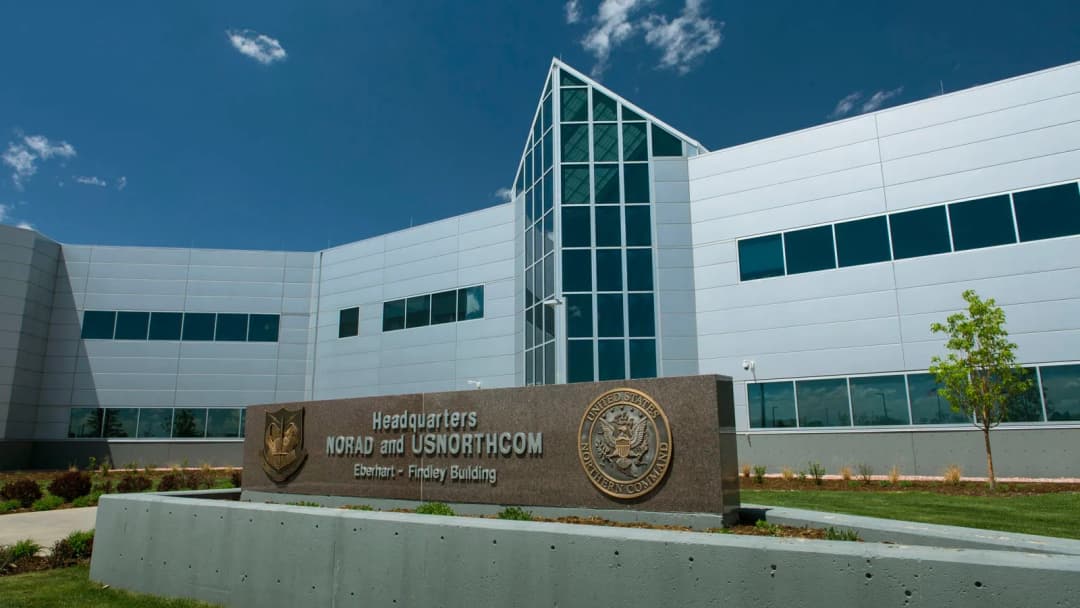 Exterior view of the Eberhart-Findley Building, headquarters for NORAD and USNORTHCOM, featuring modern architecture with large windows and a prominent stone sign in the foreground under a clear blue sky.