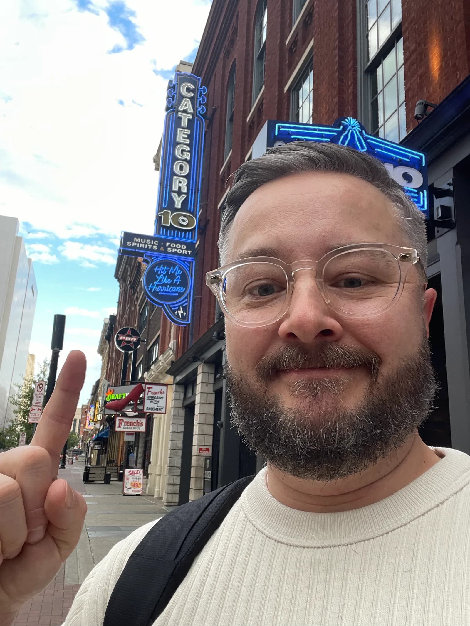 Selfie on Broadway in Nashville, pointing up at the neon Category 10 sign on a brick building.